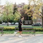 Homem corre em um parque arborizado, entre bancos e áreas urbanas, durante uma atividade física ao ar livre.