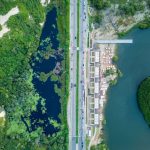 Vista aérea de trecho do litoral de Fortaleza, com faixa de areia, mar, via urbana e áreas verdes.
