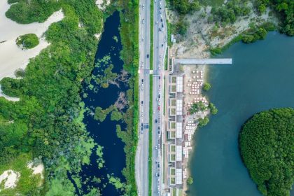 Vista aérea de trecho do litoral de Fortaleza, com faixa de areia, mar, via urbana e áreas verdes.
