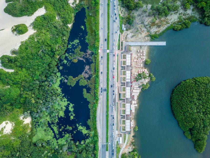 Vista aérea de trecho do litoral de Fortaleza, com faixa de areia, mar, via urbana e áreas verdes.