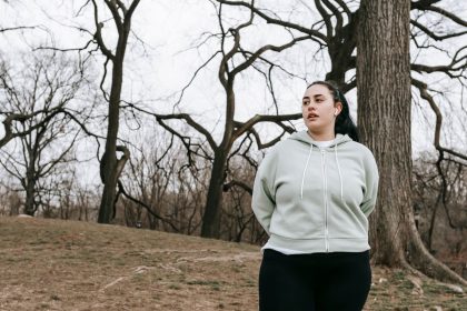 Mulher com corpo gordo, usando roupa esportiva, faz exercício em um parque durante o dia.