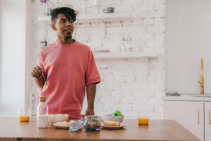 Homem prepara um café da manhã saudável com diversos ingredientes em uma cozinha moderna.