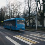 Ônibus elétrico azul trafega por uma via urbana, com árvores e edifícios ao fundo.