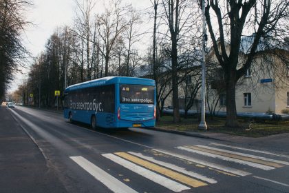 Ônibus elétrico azul trafega por uma via urbana, com árvores e edifícios ao fundo.