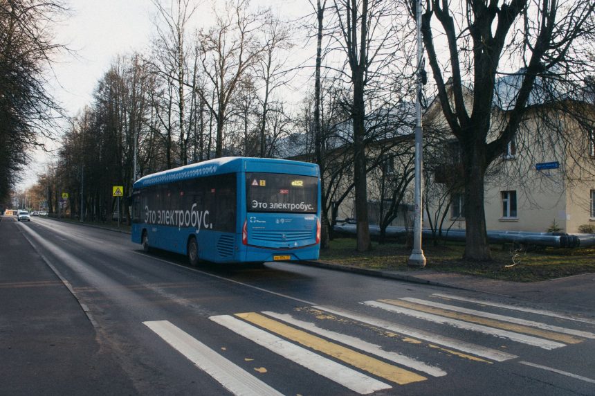 Ônibus elétrico azul trafega por uma via urbana, com árvores e edifícios ao fundo.